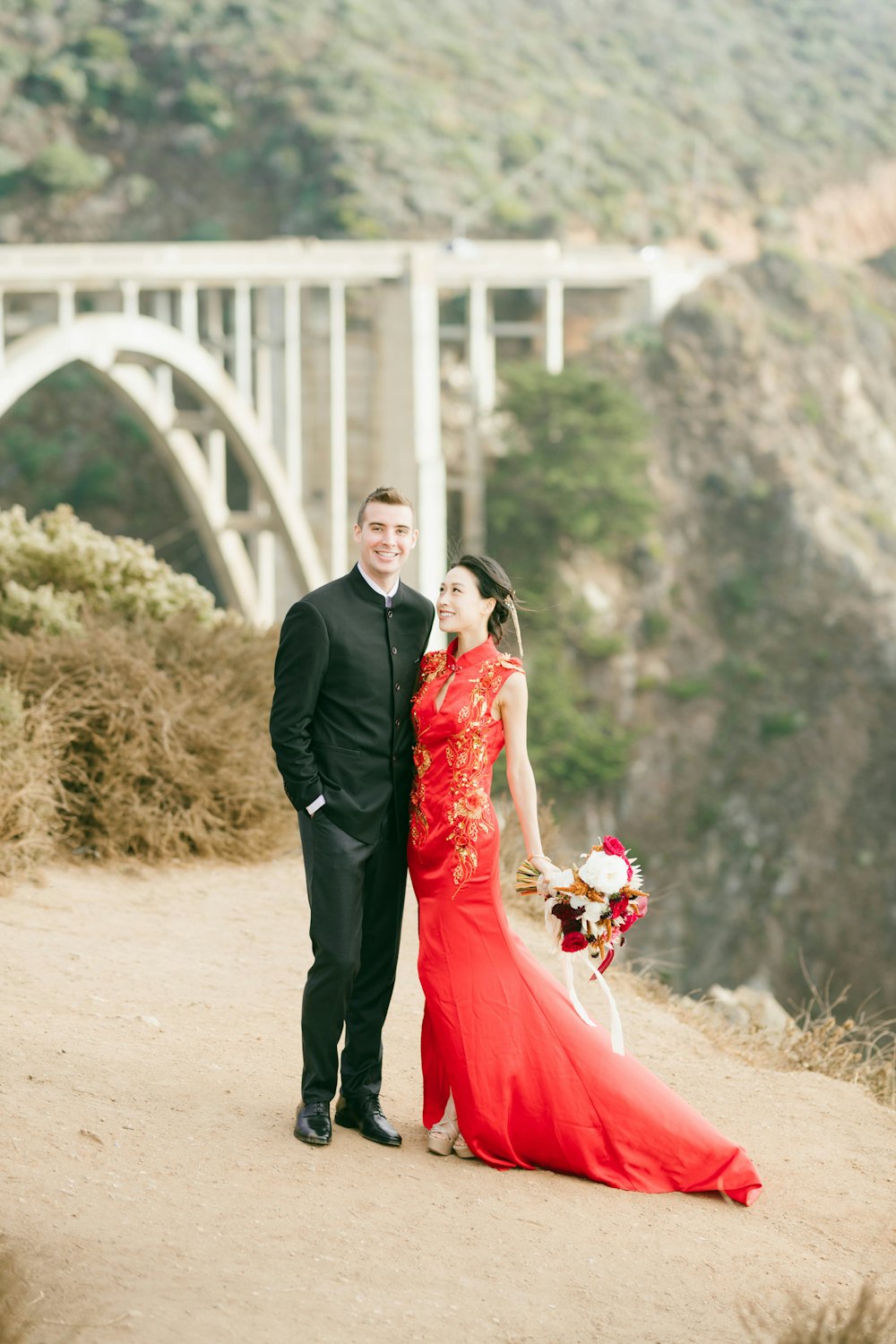 Couple on a cliff path with an arched bridge behind them